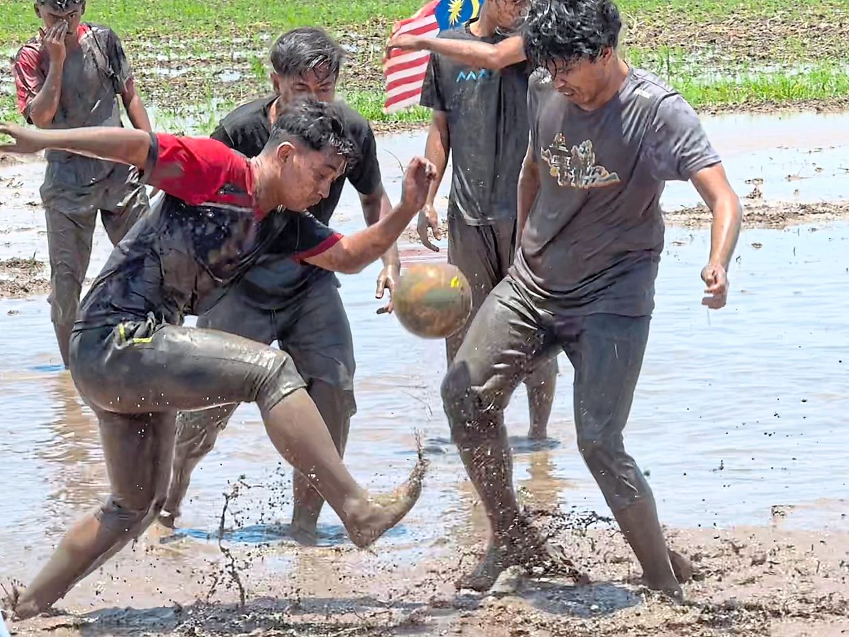 Boys having a muddy good time playing football in the slushy paddy field.