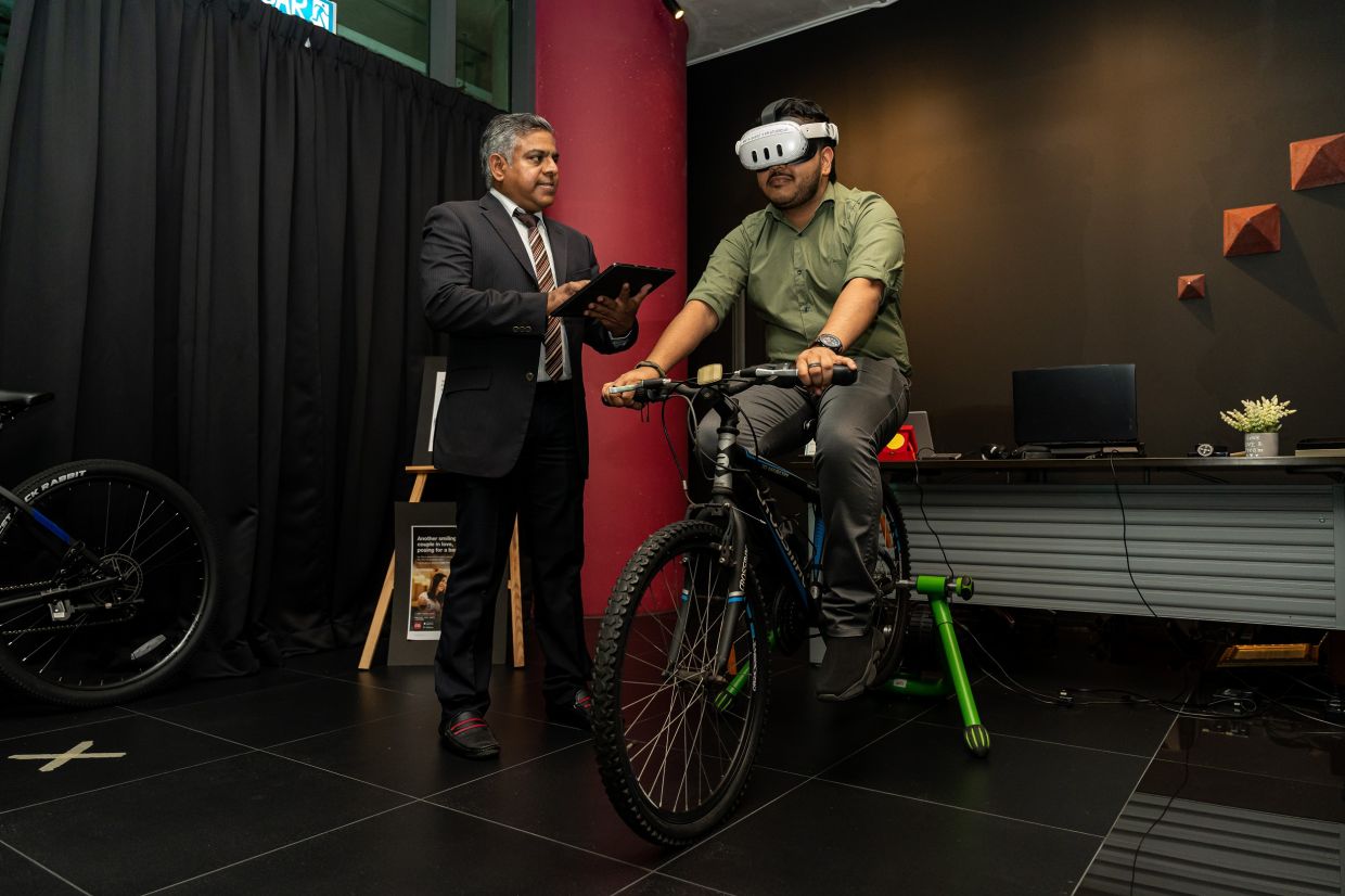 Prof Vinesh (left) at the VR Cycling Training Set facility in APU’s XR Studio. — APU