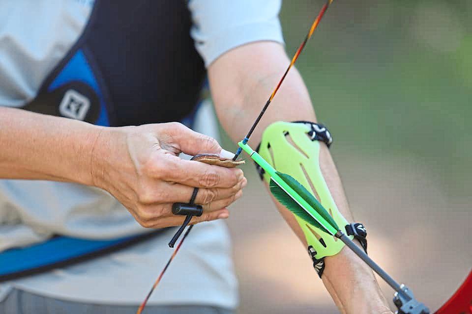 A close-up view of an archer using a tab to grip a bow string.