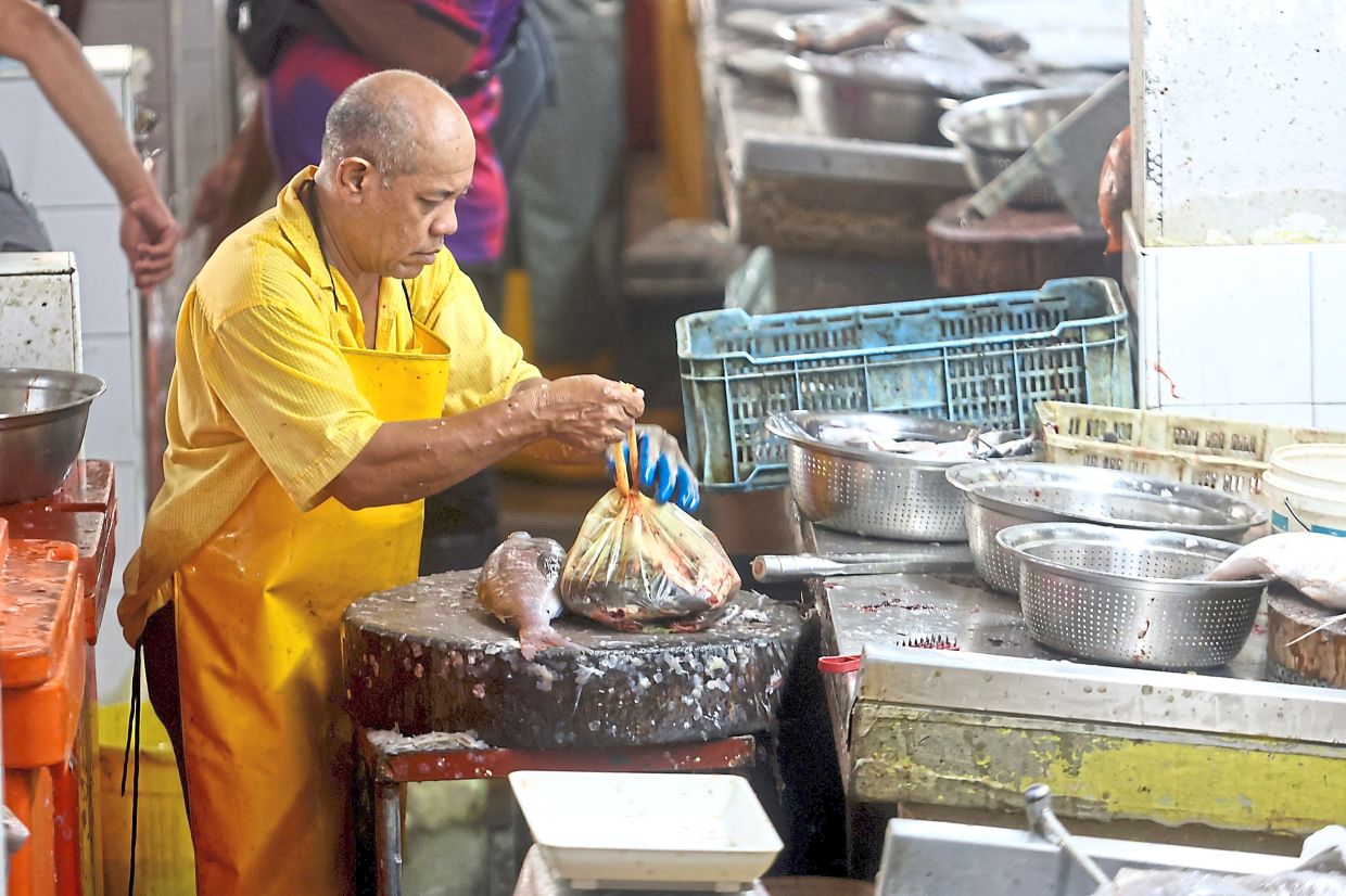 A fishmonger using a plastic bag to pack fish for a customer at Chowrasta Market.