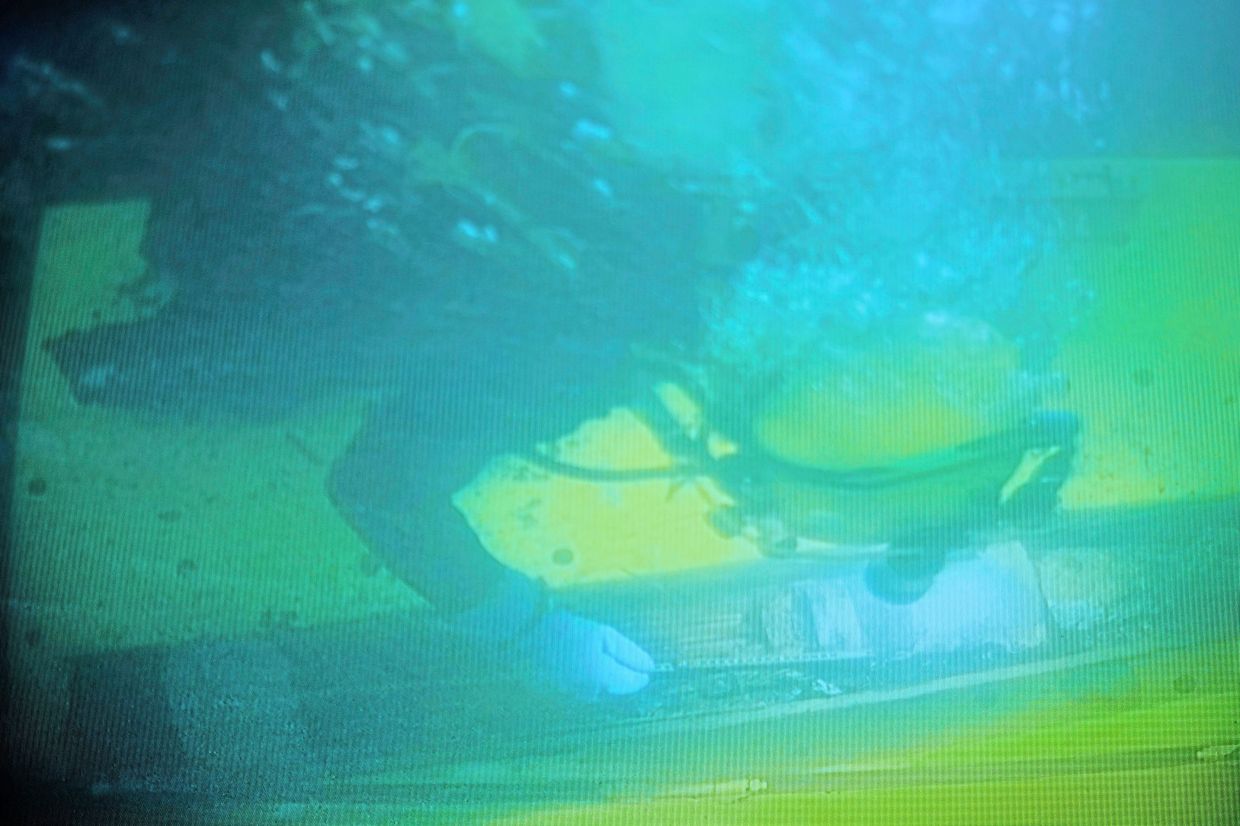 In this photo taken from a surveillance monitor, a diver is seen working on retrieving a 128mm artillery grenade.