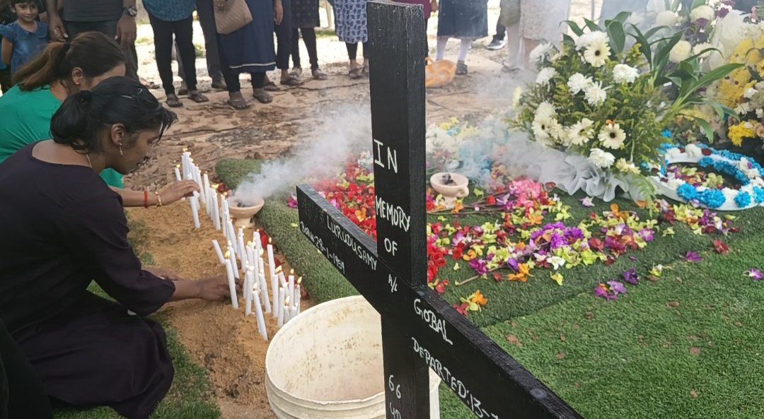 K. Datchinamurthy's sister, K. Logesh (left) lighting a candle and praying for her brother during his funeral at the Ulu Tiram Catholic Cemetery here yesterday (Sept 27).
