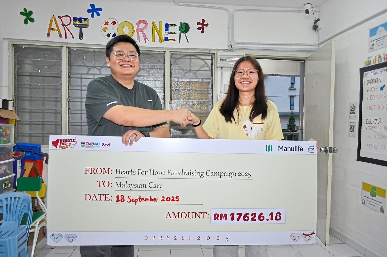 Lee (right) presenting a mock cheque of funds raised to Malaysian Care community development manager Nicholas Goh.