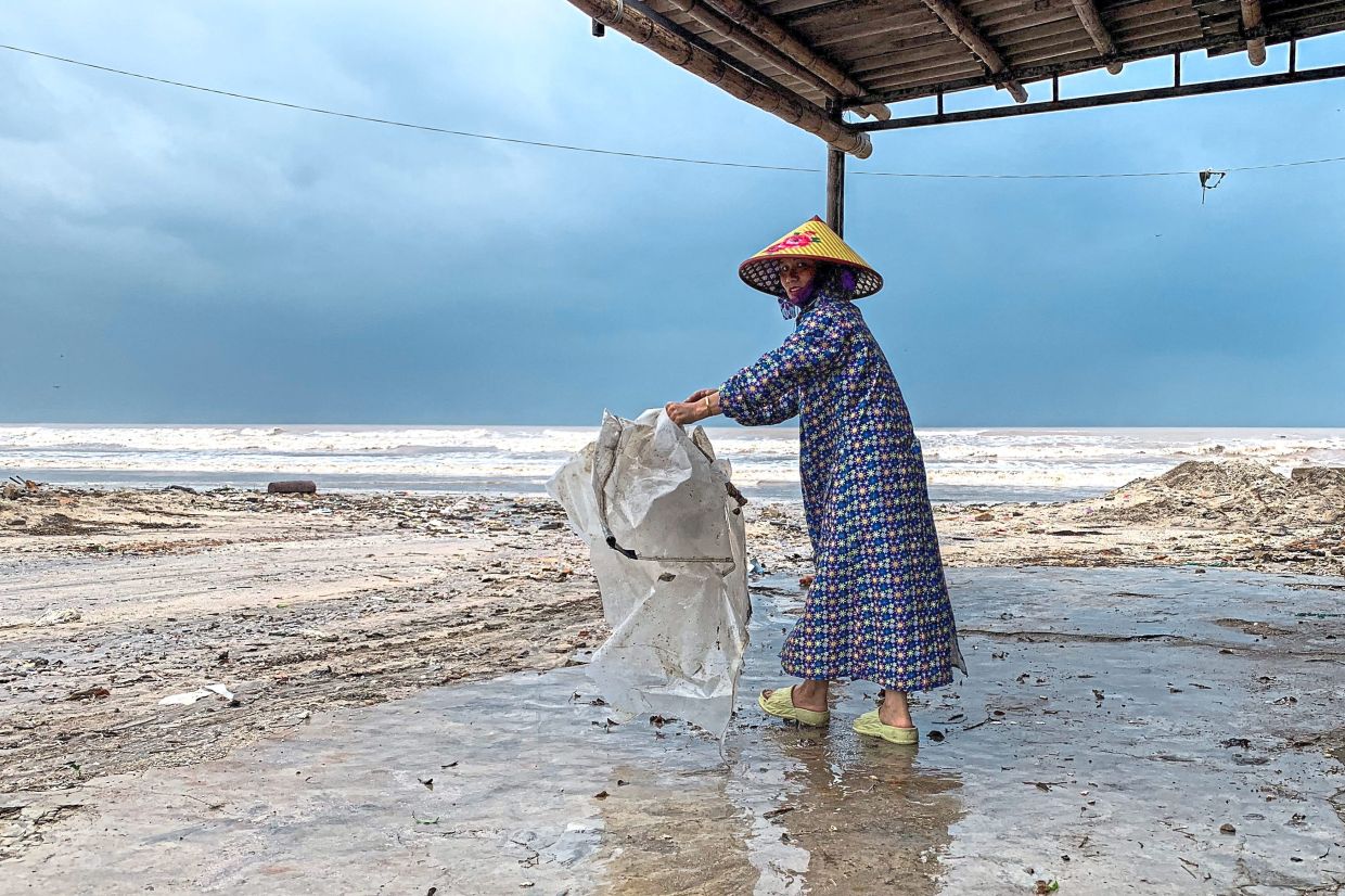 A woman wearing a raincoat collecting a plastic bag near a beach. — AFP/Reuters/AP