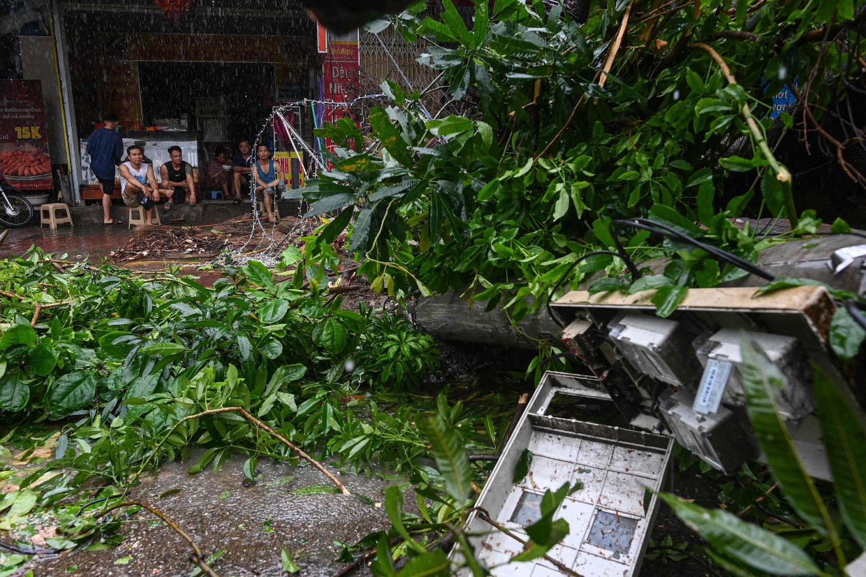 People sitting on the sidewalk past a fallen utility pole and tree branches toppled during Typhoon Bualoi's passage in Nghe An province on Sept 29. - AFP