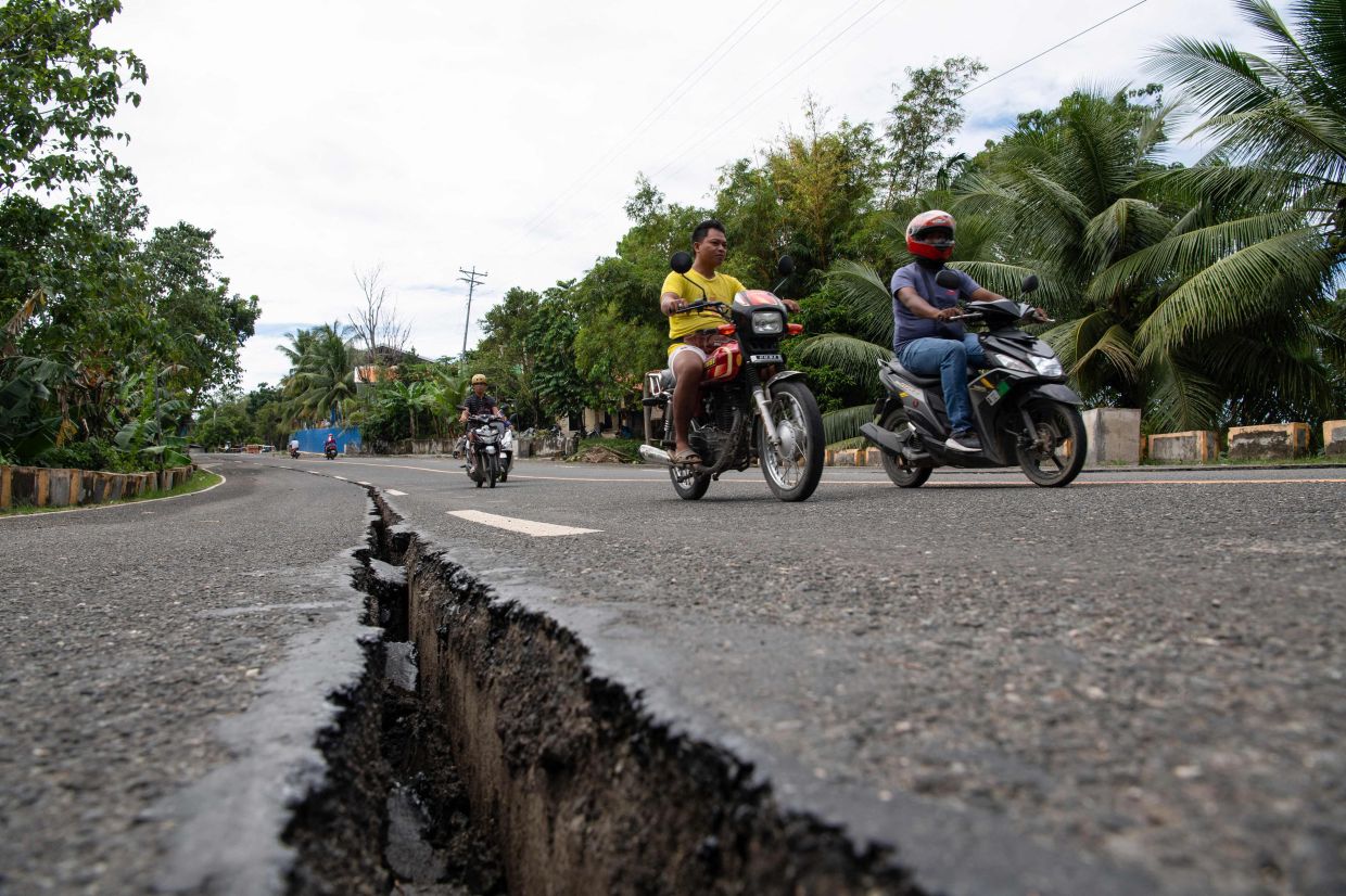 Motorists passing a crack in the road along a major highway in Tabogon town, Cebu province on Oct 1. - AFP