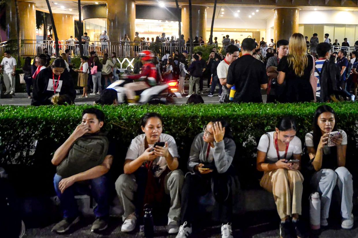 Call centre employees surfing mobile phones as they gather outside their office building after earthquake tremors at Cebu in central Philippines on Sept 30, 2025. - AFP