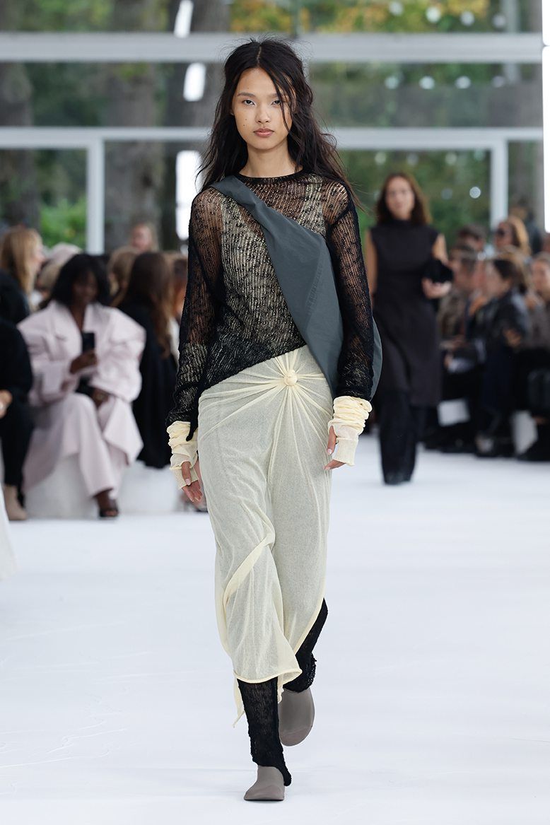 A tight knot cinching the beige dress worn under a sheer black top stands out as a design highlight. Photo: Issey Miyake