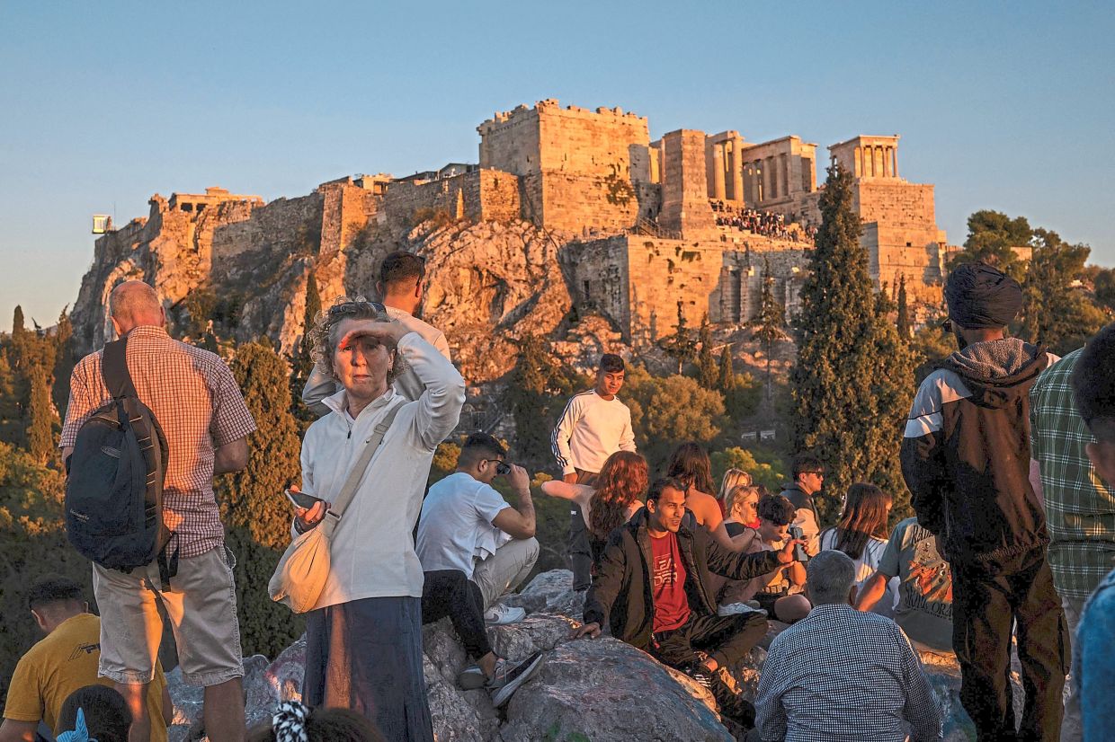 Tourists enjoying a sunset as they sit on Areopagus hill in Athens. — AFP