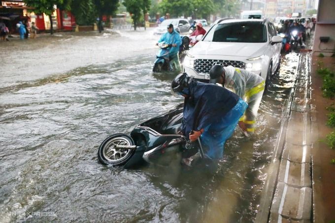 A man receives assistance after falling off his motorbike on a flooded street in Hanoi, on Sept. 30, 2025. -- Photo by VnExpress/Tung Dinh