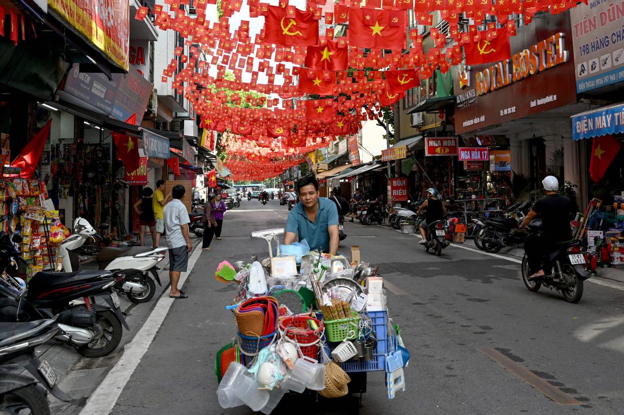A street vendor pushes his cart under flags of Vietnam and the country's Communist Party in Hanoi.-- Photo by Nhac NGUYEN / AFP