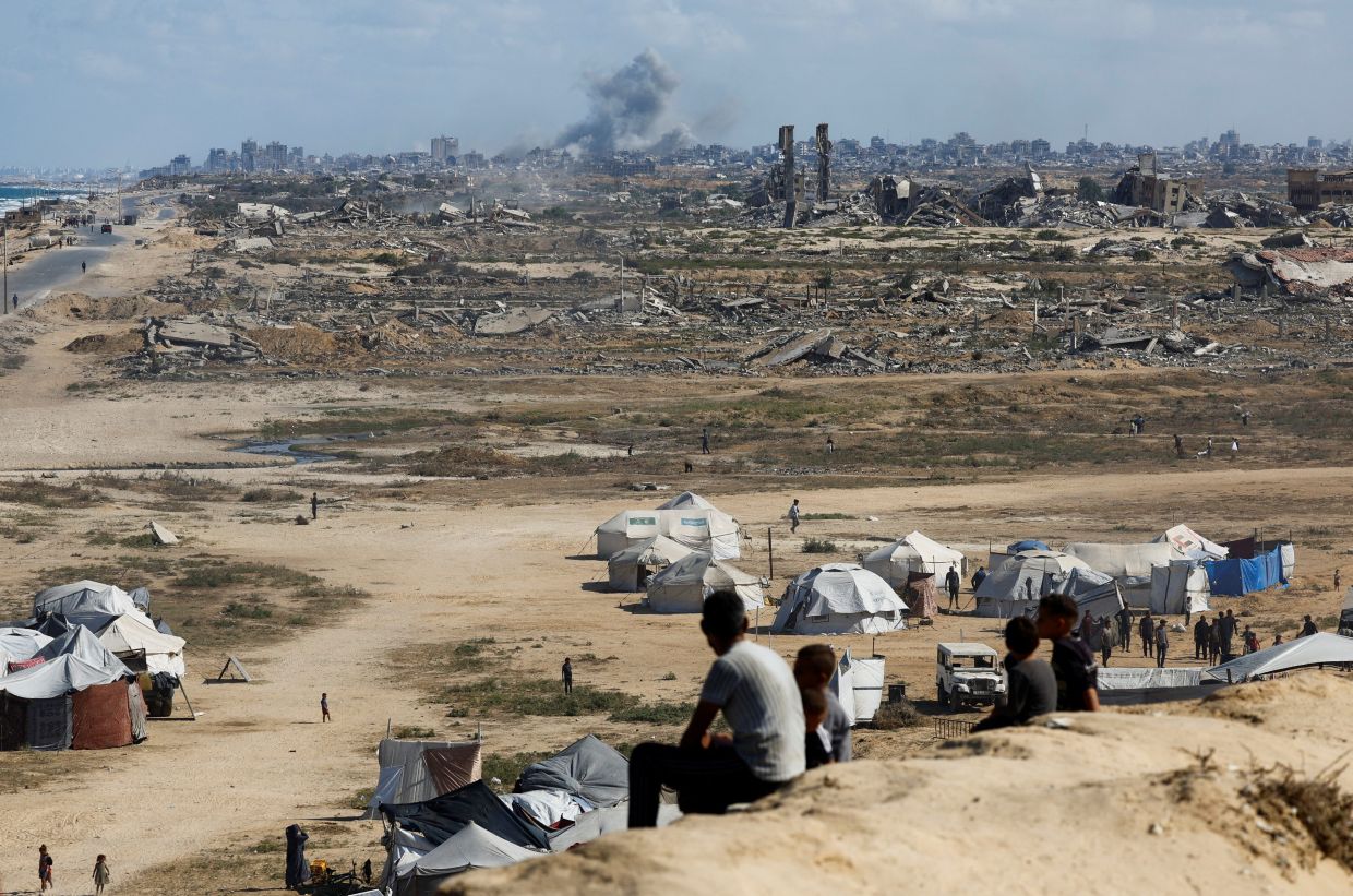 Palestinians look on as smoke rises following explosions in Gaza City, as seen from the central Gaza Strip on Sunday, October 5, 2025. -- Photo: REUTERS/Mahmoud Issa