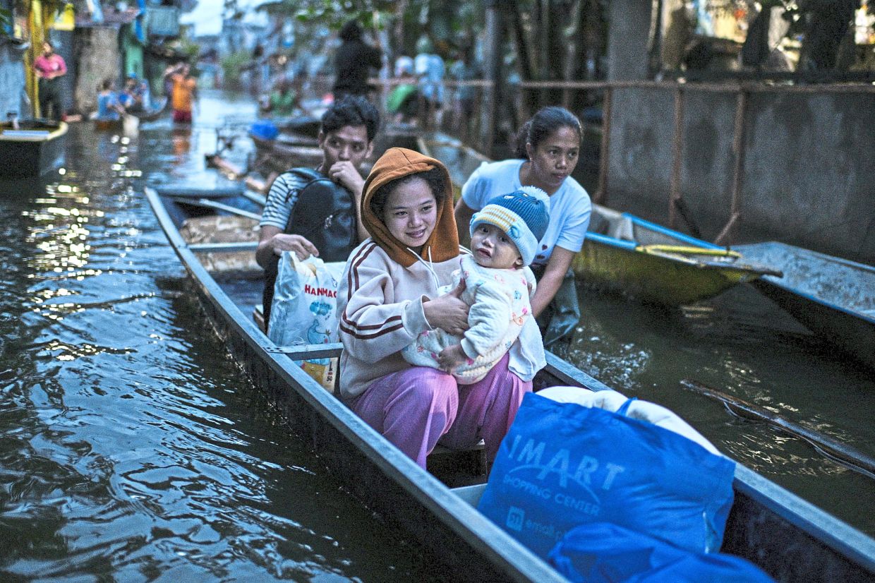Brought to safety: People riding on a boat to cross a flooded street following rains, intensified by Severe Tropical Storm Bualoi, in Dela Paz. — Reuters