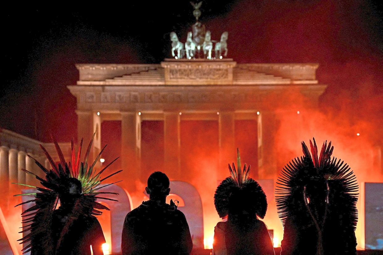 Indigenous representatives from Brazil stand in front of the projection onto giant illuminated letters with the word 'Amazonas', to highlight plight of rainforest, at the Brandenburg Gate, in Berlin, Germany, last month. —Reuters