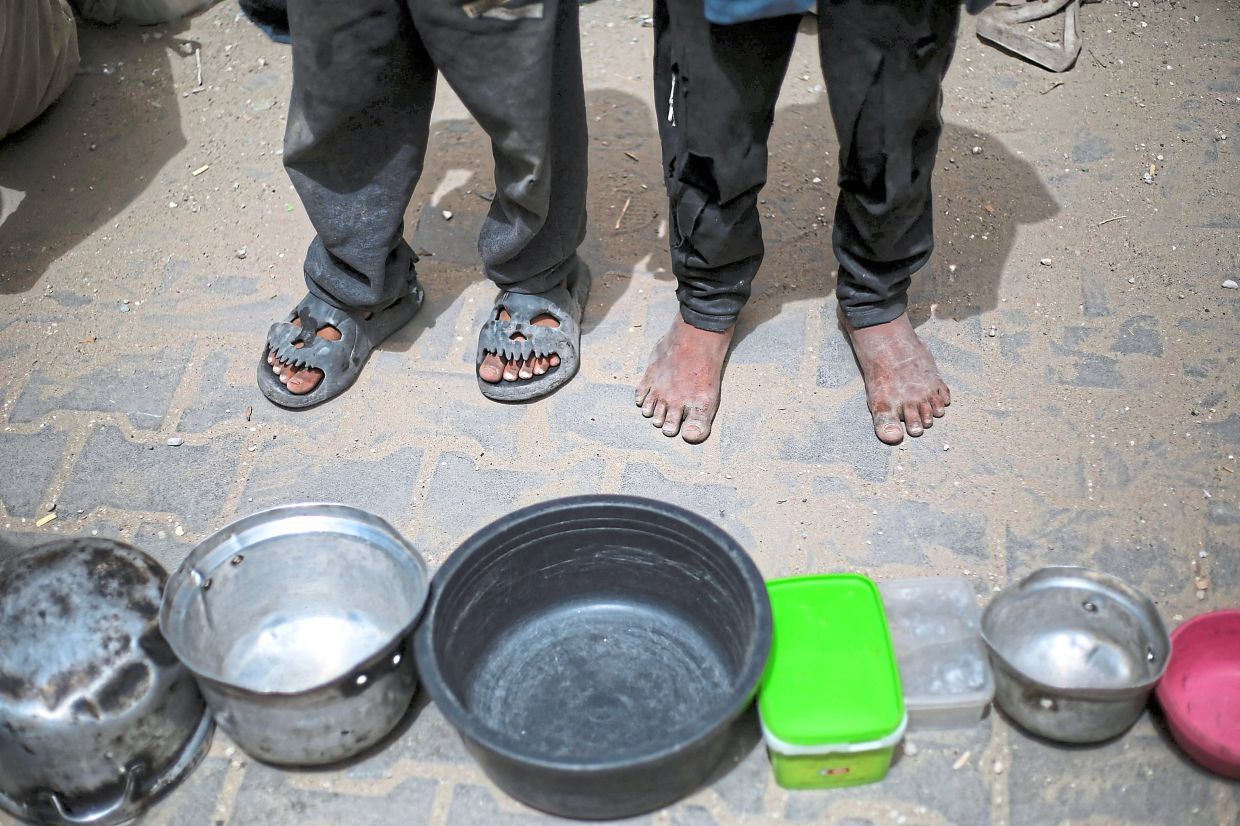 Starving Palestinian children stand over empty containers at a food distribution centre in the Nuseirat camp. — AFP