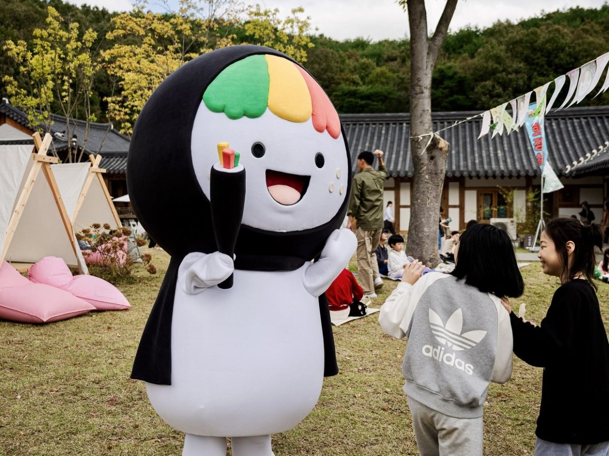 Kkodari, the gimbap mascot of Gimcheon, North Gyeongsang Province, greets visitors at the 2024 Gimcheon Gimbap Festival that has unexpectedly gone viral. Dressed as the “tail end” of a gimbap roll, the character embodies the festival’s cheeky rebrand of local identity through food and fun. - Photo: Gimcheon