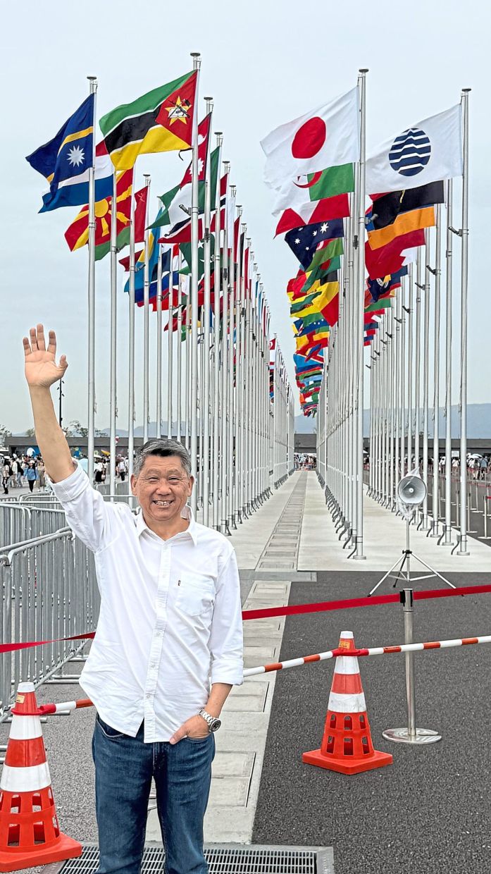 The columnist outside the Osaka Expo 2025, with flags from exhibiting countries and regions around the world in the background. 