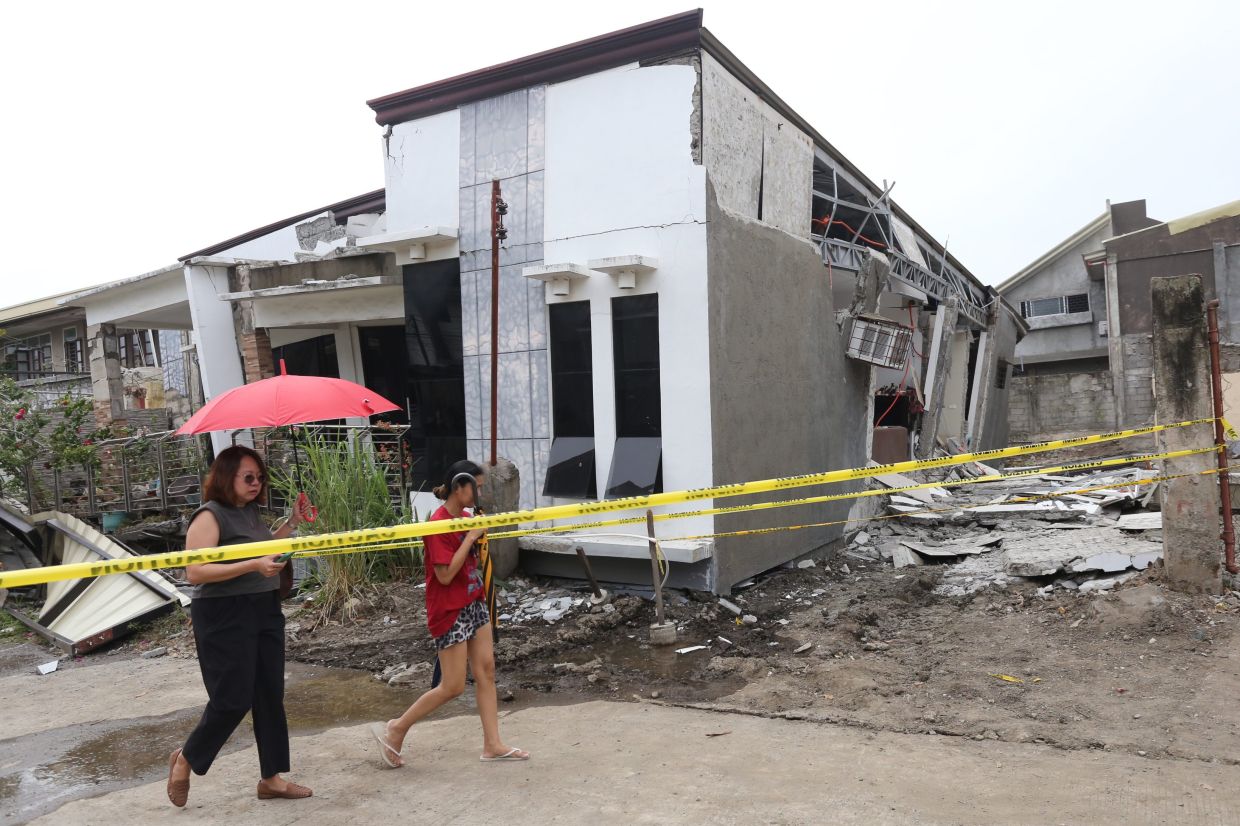 Two women walking past a damaged house after the strong earthquake in Davao City. - AP