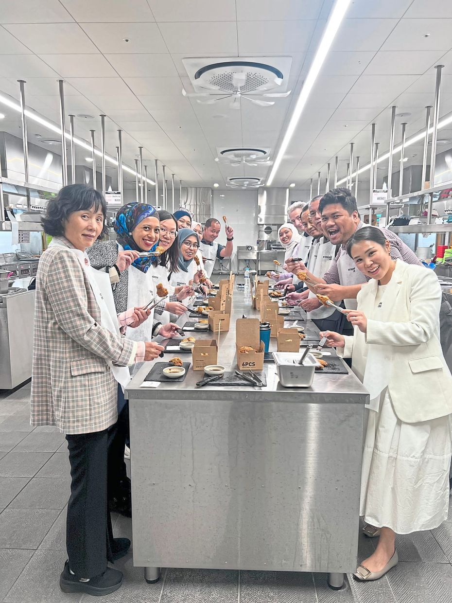 Learning how meals are prepared at Kyochon Academy, with participants saucing the chicken pieces