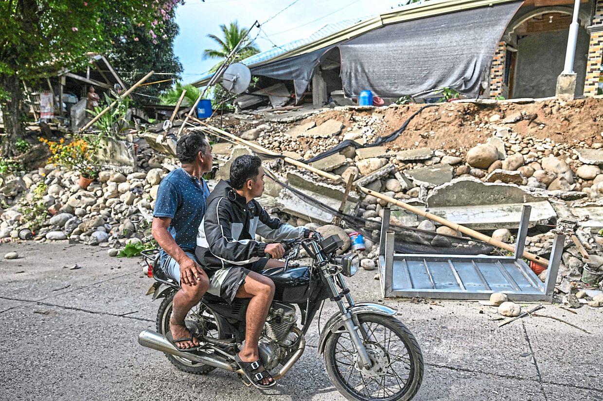 Men riding past a quake-damaged house in Manay. — AFP
