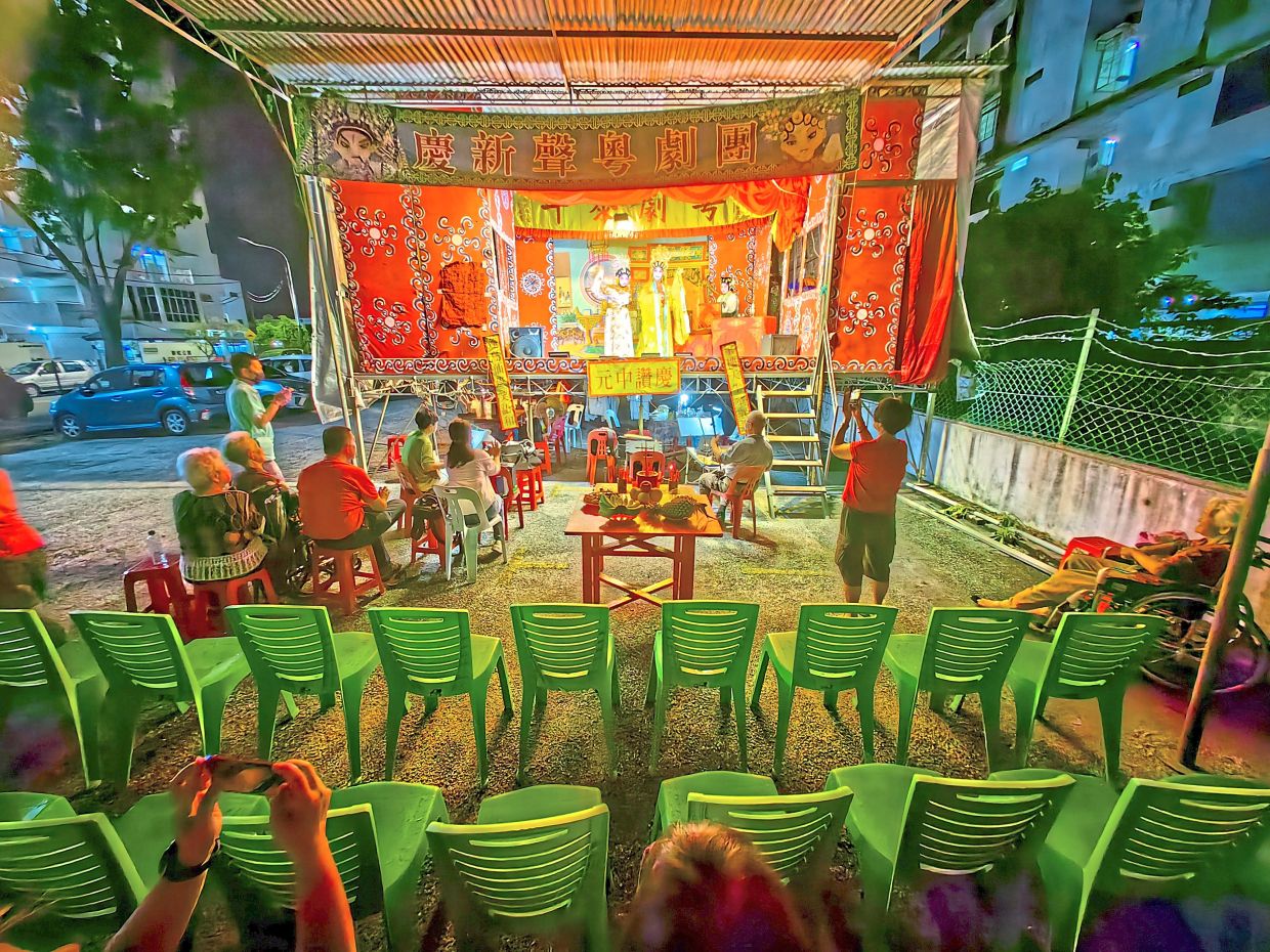 Music from traditional instruments accompanying the performance by the New Voice Cantonese Opera at Jalan Bukom in George Town. The Cantonese troupe performing before a small crowd with empty chairs in front traditionally reserved for the ‘underworld’ audience during the Hungry Ghost Festival.