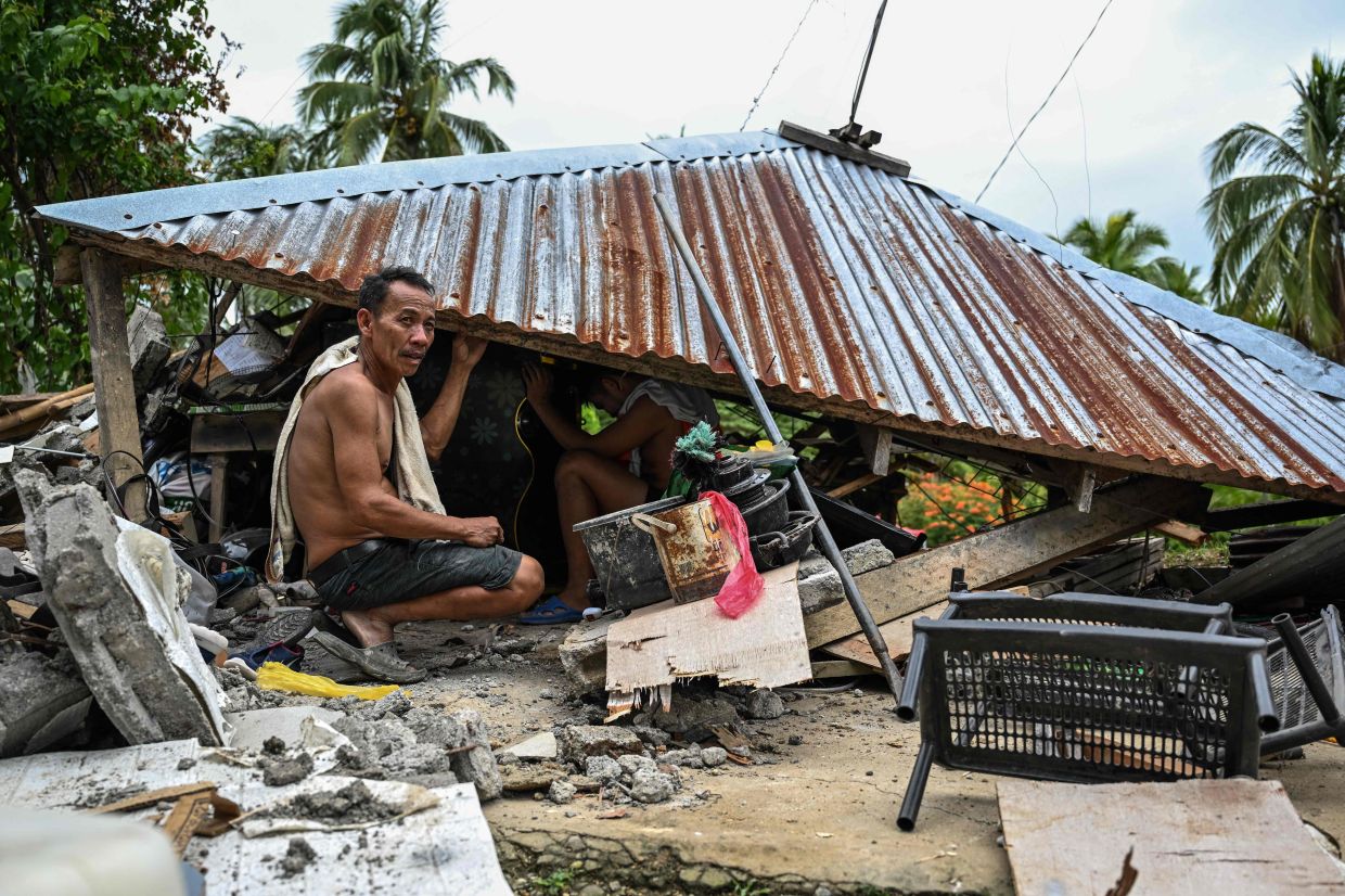 TOPSHOT - Men look for items in a collapsed house in Manay, in the province of Davao Oriental, on October 11, 2025, after two powerful quakes struck off the southern Philippines within a day, killing at least eight people and triggering tsunami warnings. -- Photo by Jam STA ROSA / AFP