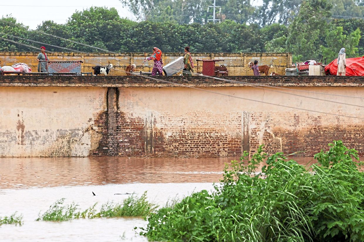 A family taking refuge on a roof of their house near Chenab River, following the monsoon rains and rising water level in Wazirabad, in Punjab.-Reuters