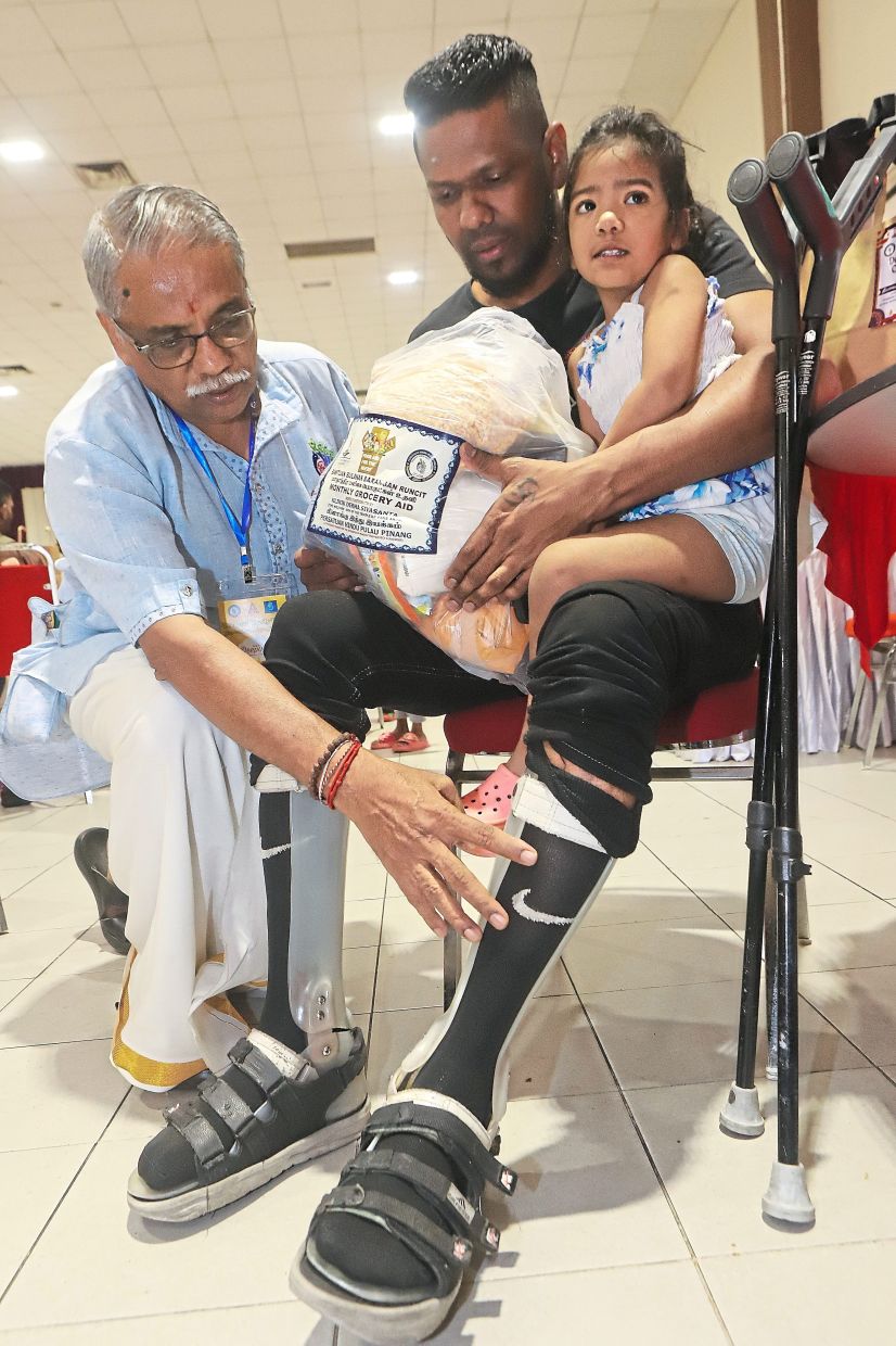 Murugiah (left) helping to adjust Jayadevan’s leg support as the latter picks up aid in Bayan Lepas.