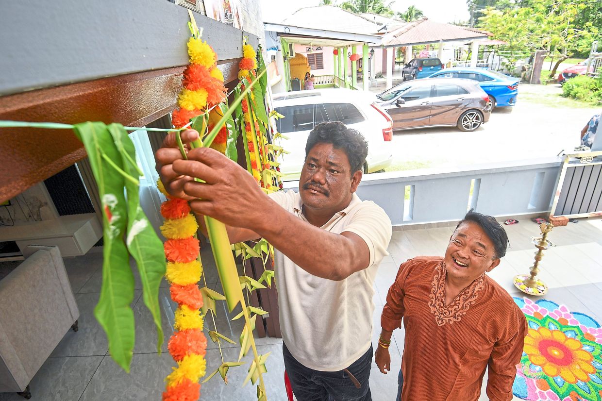 Sundar (left) and Gunaseelan work together to hang the thoranam at the doorway, a symbolic act believed to bring prosperity during Deepavali.