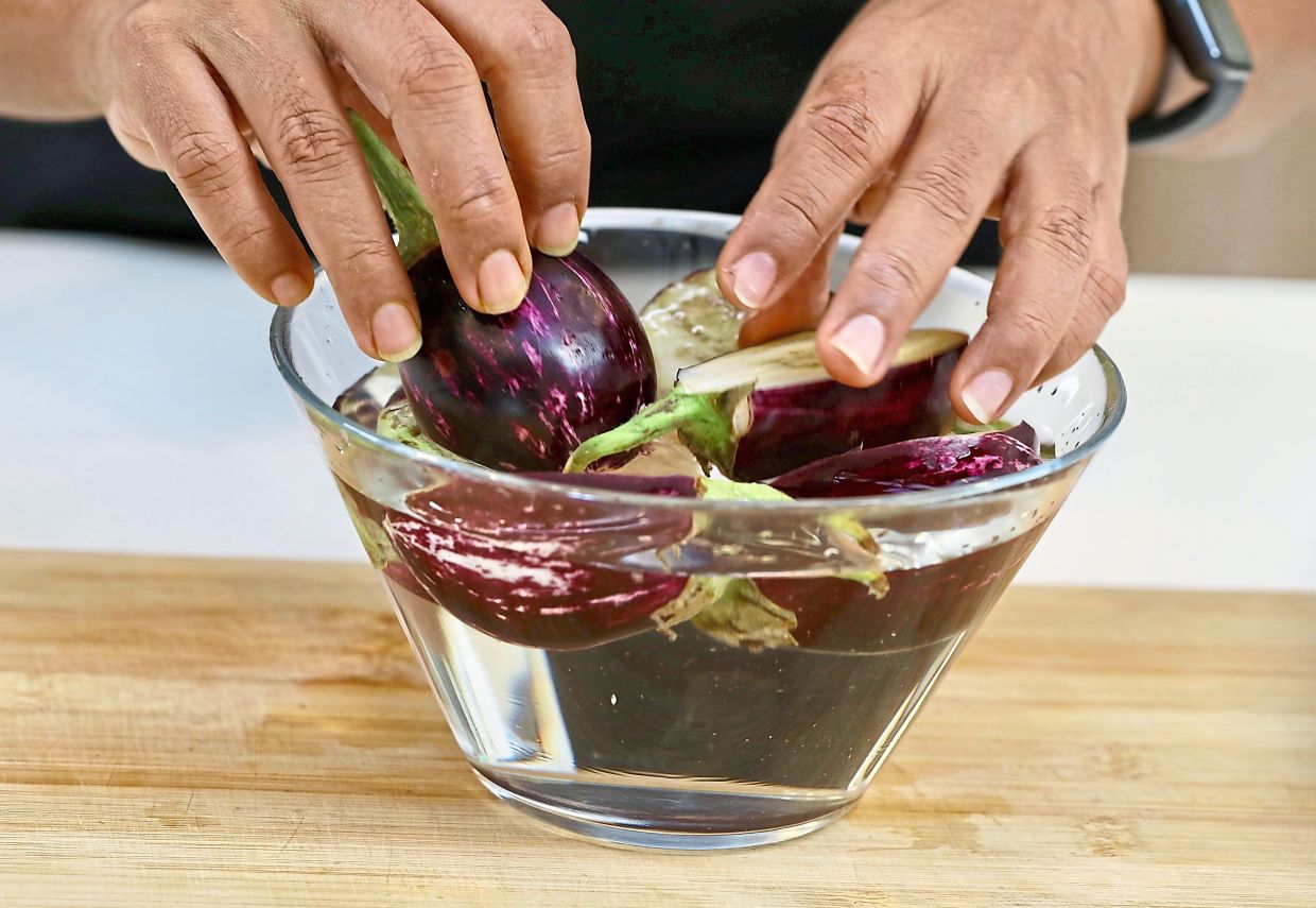Halved purple brinjal is soaked in cold water to prevent darkening.