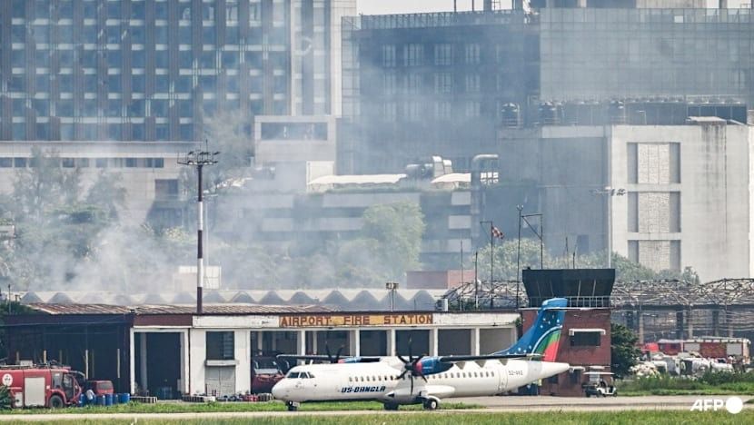 A plane prepares to take off as smoke rises from the fire-damaged cargo terminal of Hazrat Shahjalal International Airport, a day after the blaze in Dhaka. - Photo: AFP