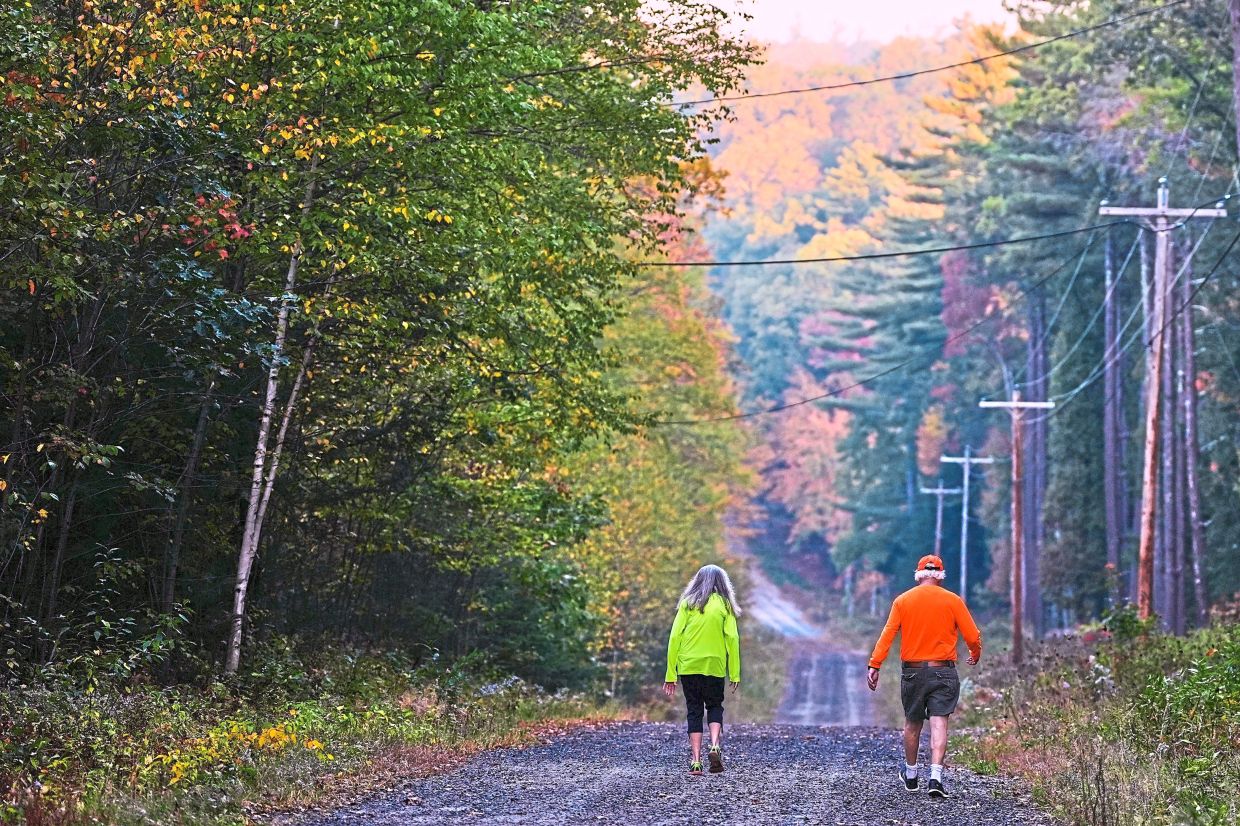 A couple walking at dawn among colourful trees in a forest in Chester, New Hampshire.