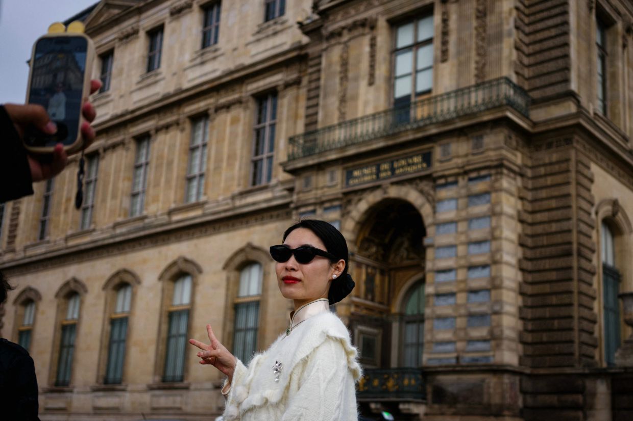 A tourist gets photographed in front of the window of the Louvre museum, through which the thieves entered to steal priceless jewels last weekend. Photo: AFP 
