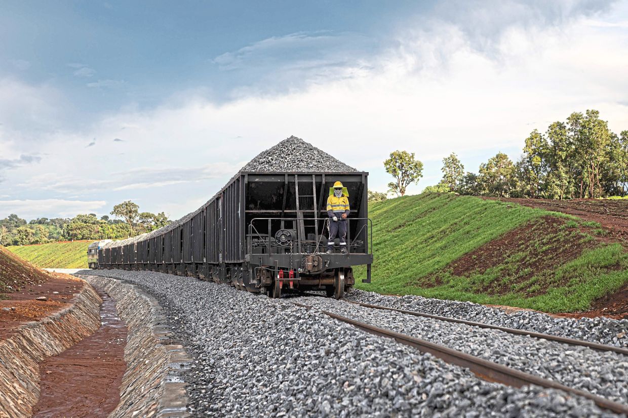 A China Railway 18th Bureau Group employee standing at the back of a train transporting rocks at the mining complex. in the Simandou mountain range in the Nzerekore region, on September 2, 2025. In the Simandou mountains of Guinea's lush rainforest, a mammoth mining project that could make the west African country one of the world's largest iron exporters is raising equal parts hope and fear.In just a few weeks, Guinea will export its first shipments of iron ore from its Simandou Project, finally cashing in on the high-grade iron deposits discovered decades ago in the country's southeast.Not only does the project potentially offer a steady stream of revenue for the impoverished country but it has also precipitated the development of key infrastructure in the region, although the opacity of contracts make it impossible to estimate the state's gains.Industrial partners have spent approximately $20 billion constructing more than 650 kilometres (400 miles) of railway and a massive port that will connect the remote region to the larger world. (Photo by PATRICK MEINHARDT / AFP)
