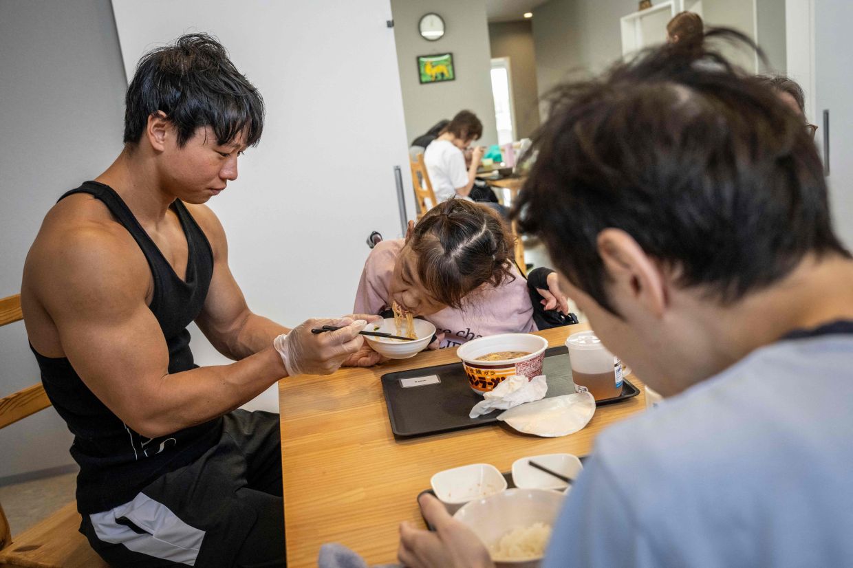 Takuya Usui helping Madoka Yamaguchi (centre) eat lunch at a care home for people with disabilities. - AFP