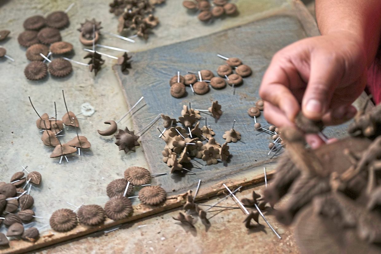 Hernandez inserts small fragile clay figures into a tree of life sculpture.