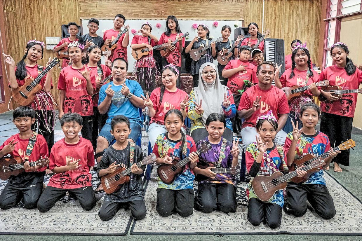 Music teacher Mastra (centre) poses with her students, who are also members of the Koleh Buskers group, at Sekolah Kebangsaan (SK) Sayong Pinang.