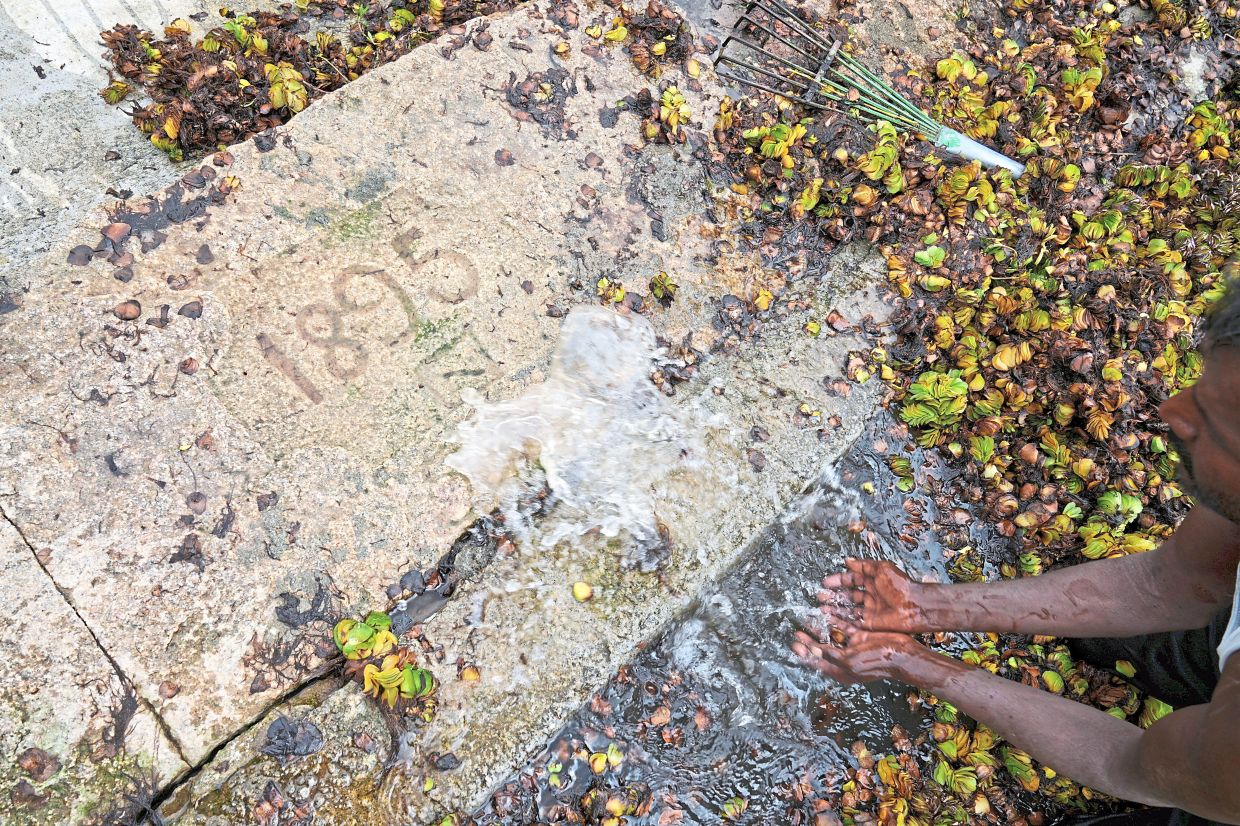 Revealing history: A worker spraying water to reveal a marking that reads 1895, the year a wall was built at Doddajala Lake. — AP