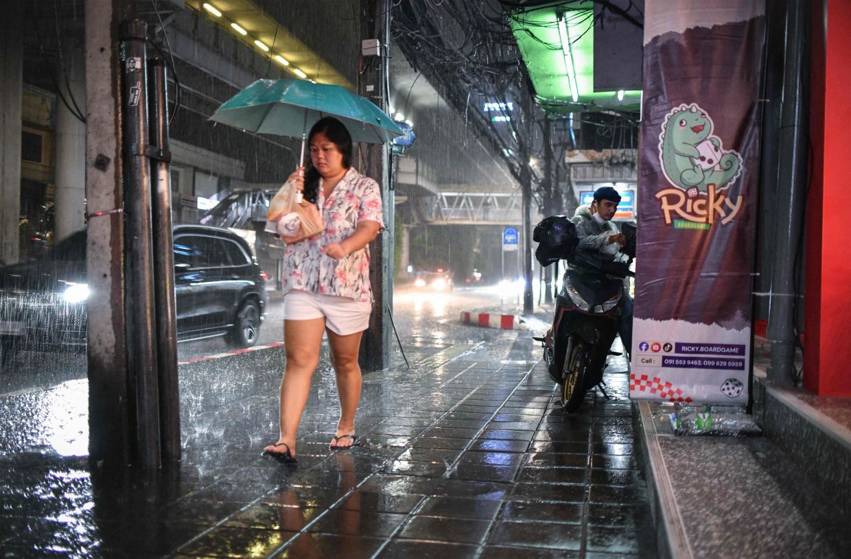 A woman walks under an umbrella to shelter from the rain along Sukhumvit road in Bangkok. -- Photo by Amaury PAUL / AFP