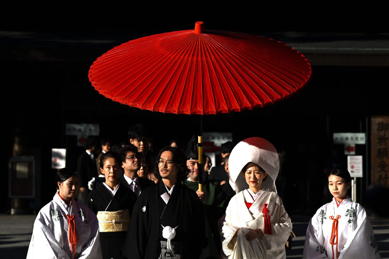 People walk under a red umbrella during a wedding ceremony at the Meiji Shrine, coinciding with the Autumn Festival on the Culture Day public holiday, in Tokyo on Monday, November 3, 2025. -- Photo by Greg Baker / AFP
