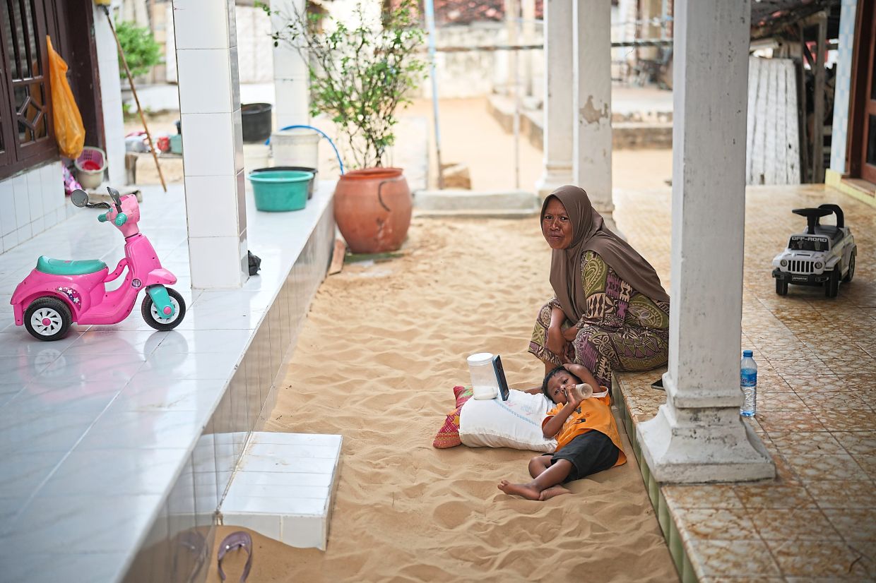 A woman looks after her son in a sandpit at home in Legung Timur village in Sumenep on Madura Island, Indonesia, Tuesday, Sept. 9, 2025. (AP Photo/Dita Alangkara)
