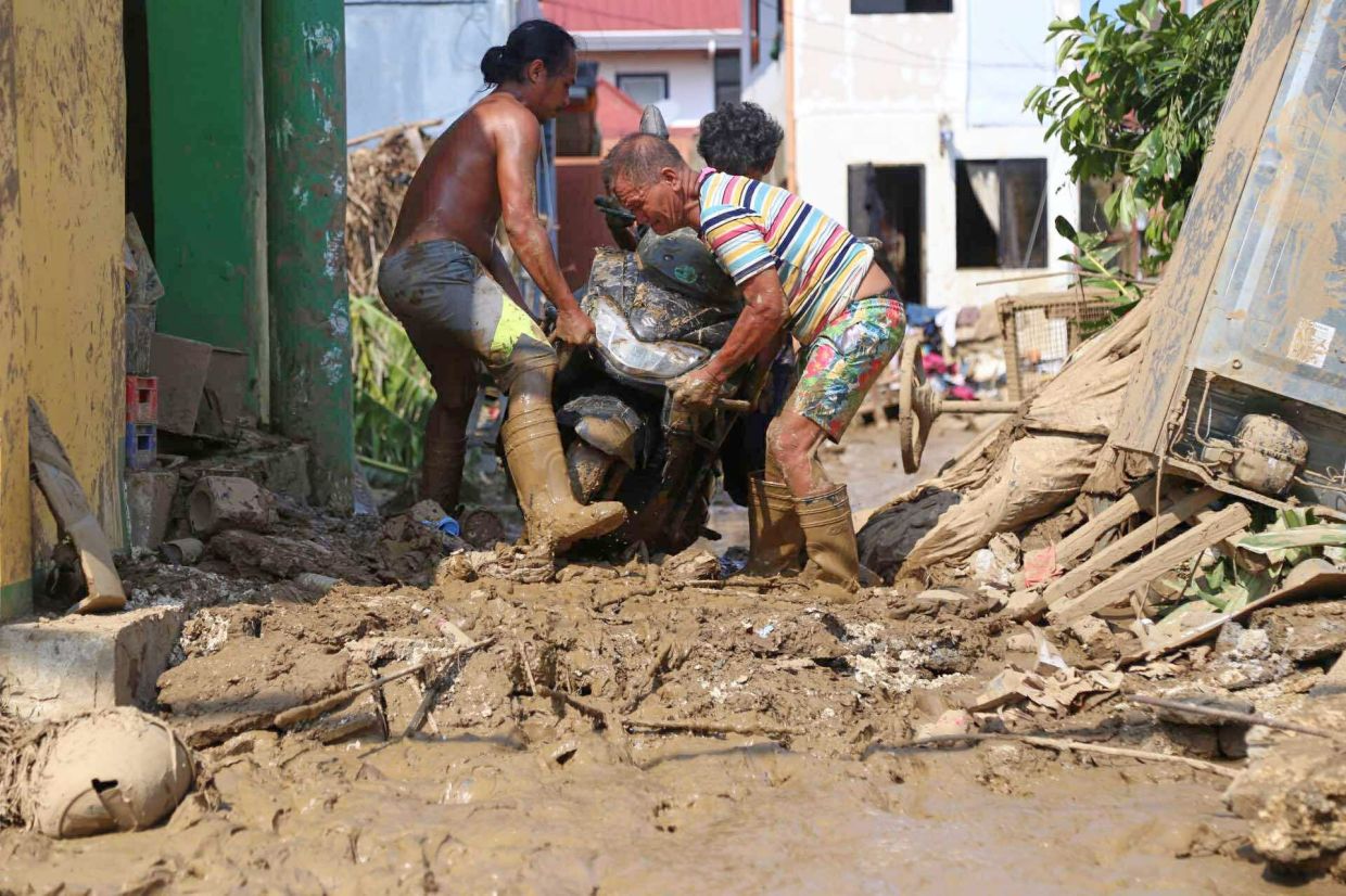 Residents carry a motorcycle along a muddied street caused by Typhoon Kalmaegi, in Liloan, Cebu province, central Philippines, on Thursday, Nov 6, 2025. -- AP Photo/Jacqueline Hernandez