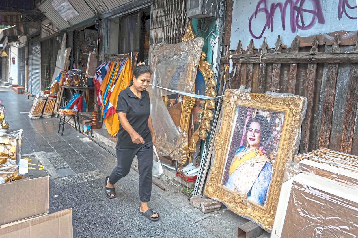 Mourning period: A woman dressed in black to mourn the death of Sirikit walking past the former queen’s portrait displayed in Bangkok. — AFP