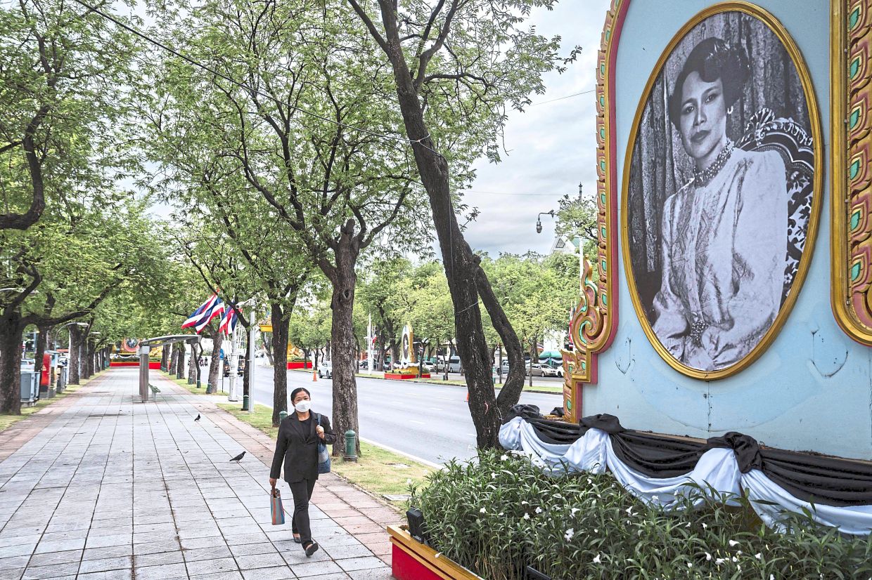 In memory: People using escalators past a screen displaying a message mourning Sirikit’s passing at a mall in Bangkok. (Below) A woman dressed in black to mourn Sirikit’s passing walking past her portrait displayed on a street in Bangkok. The government has declared a year-long mourning period for officials and urged the public to wear traditional Thai mourning colours of black or white for 90 days. — AFP