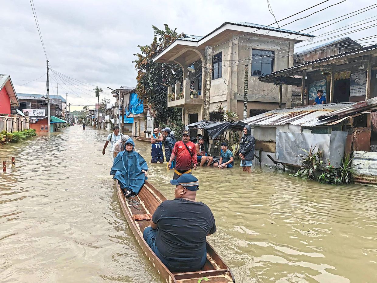 Better safe than sorry: Town officials riding in a boat to inspect a flooded street in Jipapad, Eastern Samar province. (Right) Residents evacuating from their homes ahead of the arrival of Fung-wong in Tuguegarao City, Cagayan province. — AFP