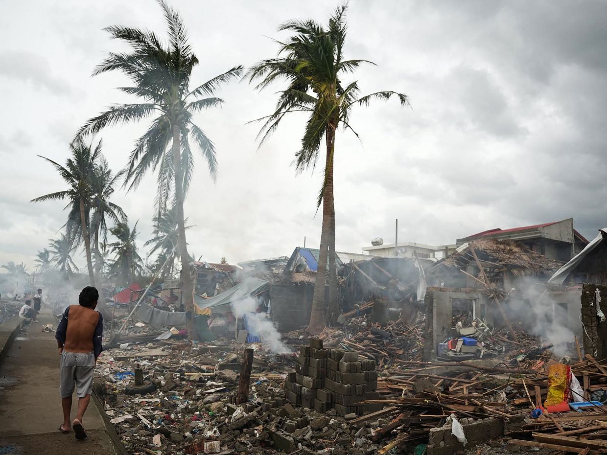 Residents burn wood from their destroyed houses near the seawall at Garchitorena in Camarines Sur province, south of Manila, on Monday, November 10, 2025, a day after Super Typhoon Fung-wong made landfall. -- Photo by Charism SAYAT / AFP