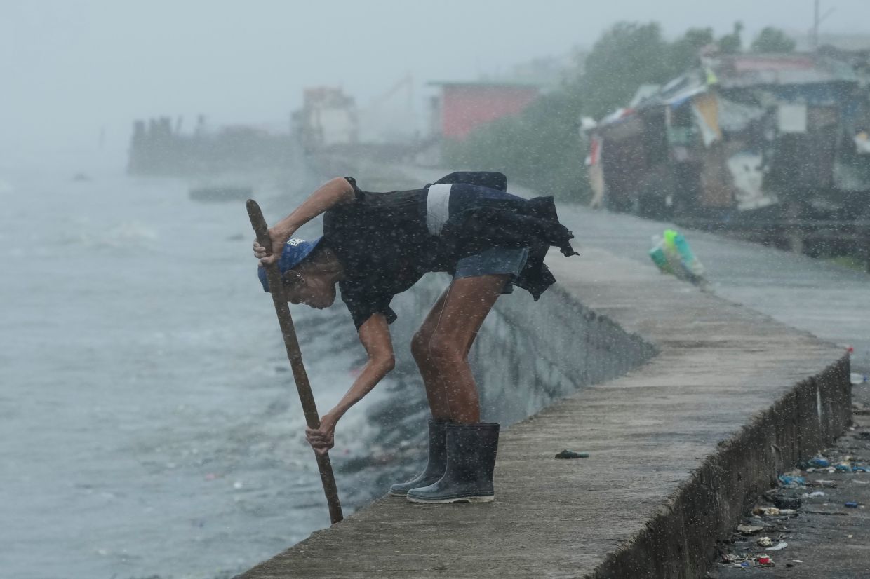 A woman uses a stick with a net to collect plastic bottles during heavy rain due to Typhoon Fung-wong along a coastal village on Monday, Nov. 10, 2025, in Navotas, Philippines. -- AP Photo/Aaron Favila