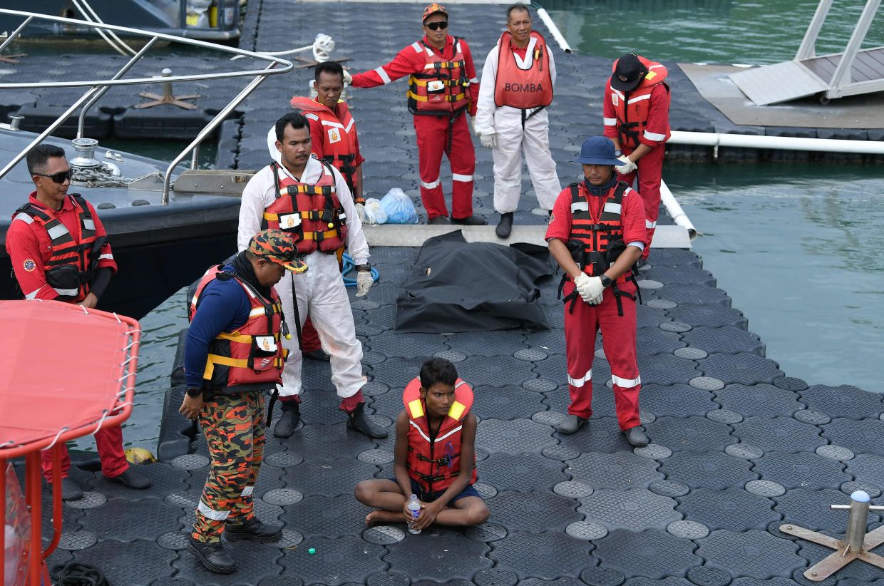 Rohingya migrant Iman Shorif (centre) drinks water as he sits after his rescue at a jetty, days after his boat carrying migrants from Myanmar capsized near the Malaysia-Thailand border, in Langkawi on November 11, 2025. Authorities in Malaysia and Thailand have recovered at least 21 bodies as they search for survivors after a boat carrying undocumented migrants capsized, police and maritime officials said on November 10.-- Photo by Hakim Mustapha / AFP