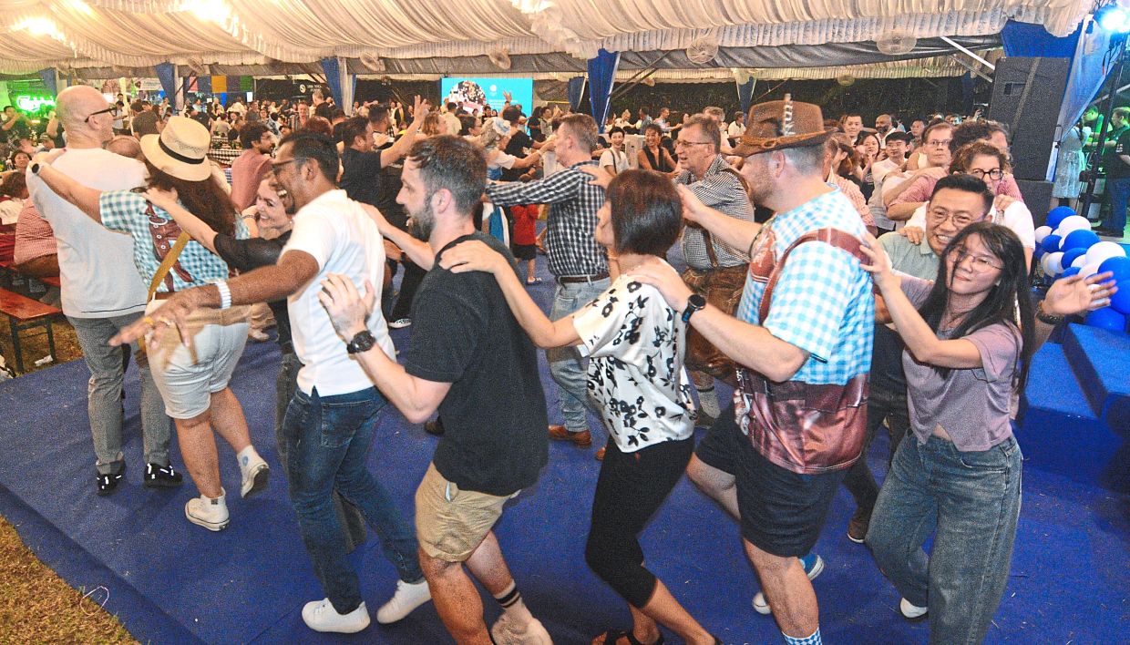 Revellers forming a conga line that snakes around the canopy venue of the Oktoberfest 2025 celebrations.