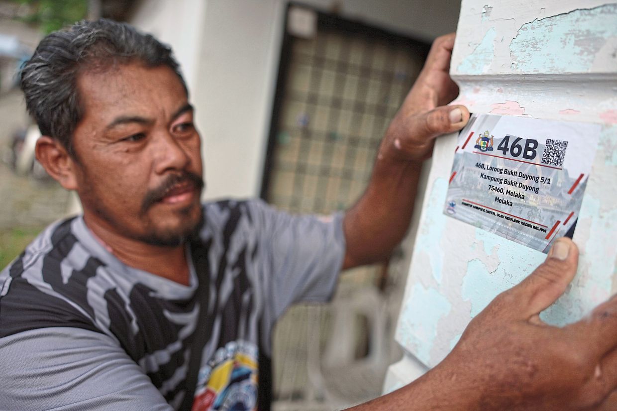 Mohamad Rizal affixing the Digital Village QR code at his home in Kampung Bukit Duyong.